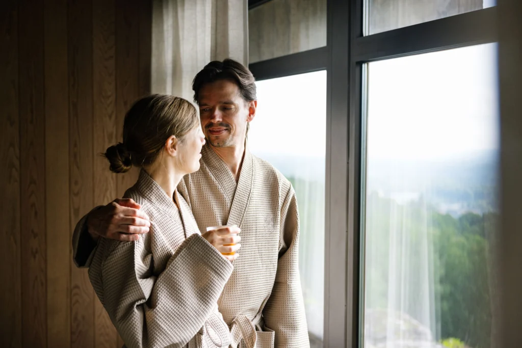 Ett par som håller om varandra vid ett fönster på earth spa på Billingehus